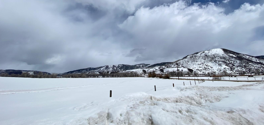 A snow covered field sits quietly with mountains in the background