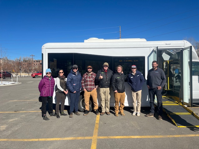 People stand and pose for a photo in front of an electric shuttle in a parking lot.