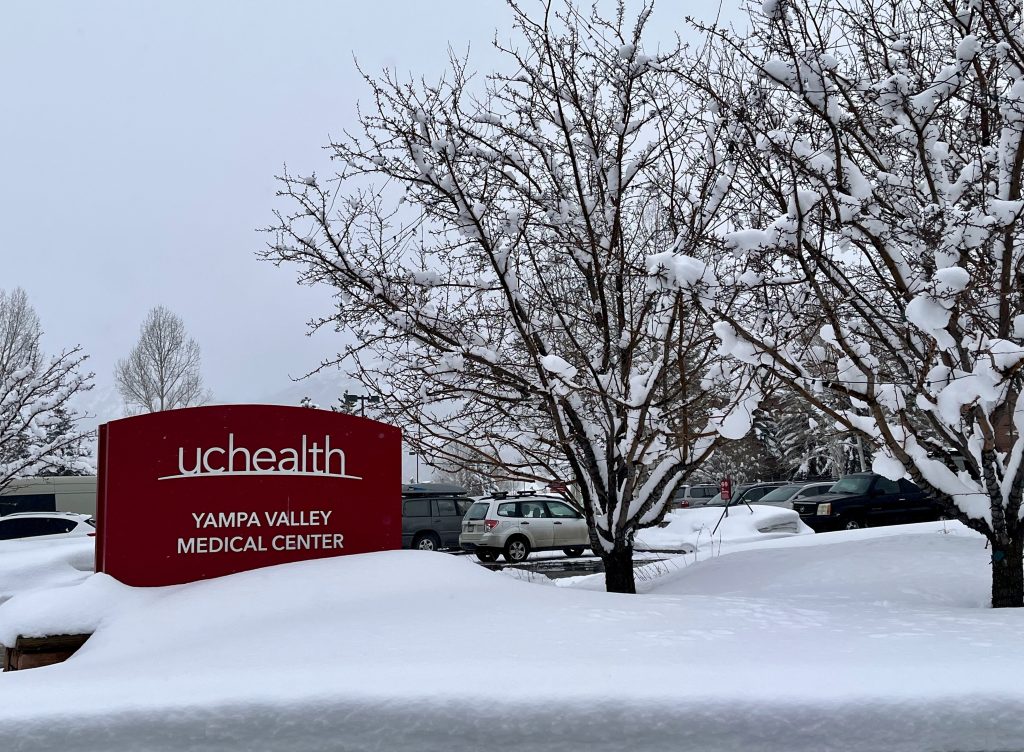 UCHealth sign outside entrance surrounded by snowy trees.