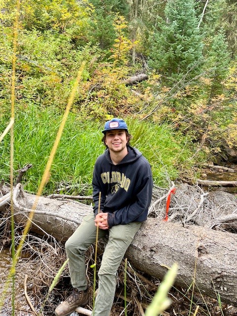 Image of Ben Cavarra sitting on a log by the river.