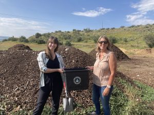 Two people standing in front of compost pile with a Cowgirl Compost bin. Cowgirl is part of CGBN-YV.