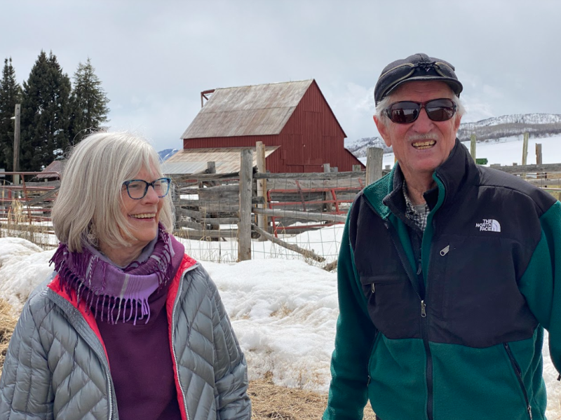 Gael and Jay Fetcher stand, smiling on their ranch with snow in the background.