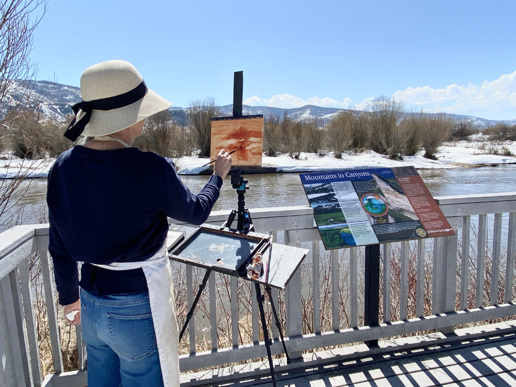 Back of plein air painter overlooking a river with snow and cottonwoods on the banks.