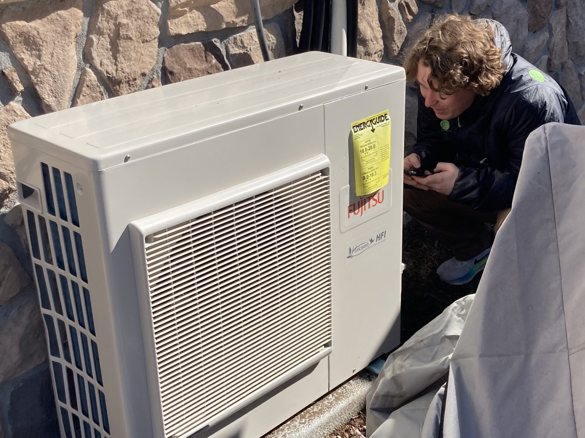 A person crouching and looking at a heat pump