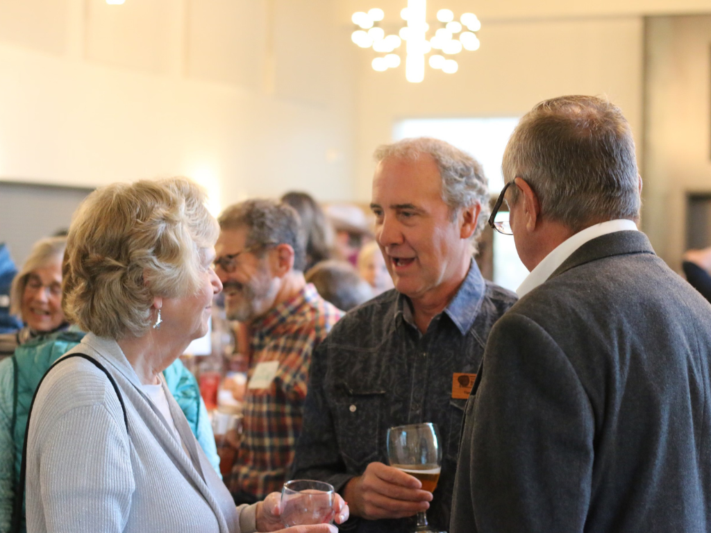 A man stands speaking to two people in a crowded room.